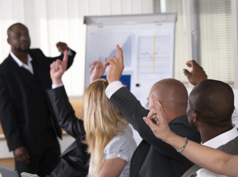 A diverse group of people engaged in a business presentation, raising hands to ask questions.